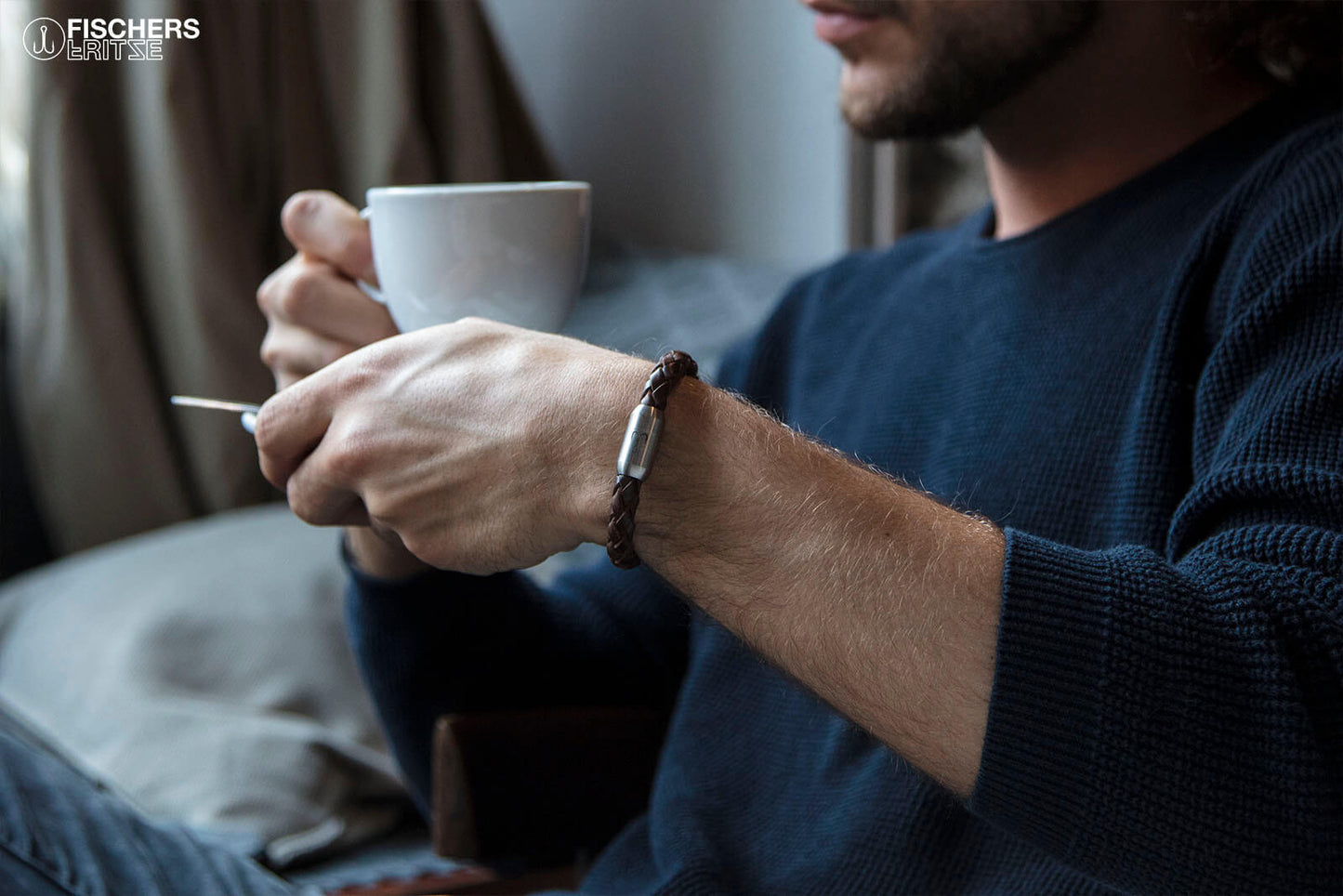 Mann hält Kaffeetasse und traegt Lederarmband mit graviertem Magnetverschluss silber von Fischers Fritze