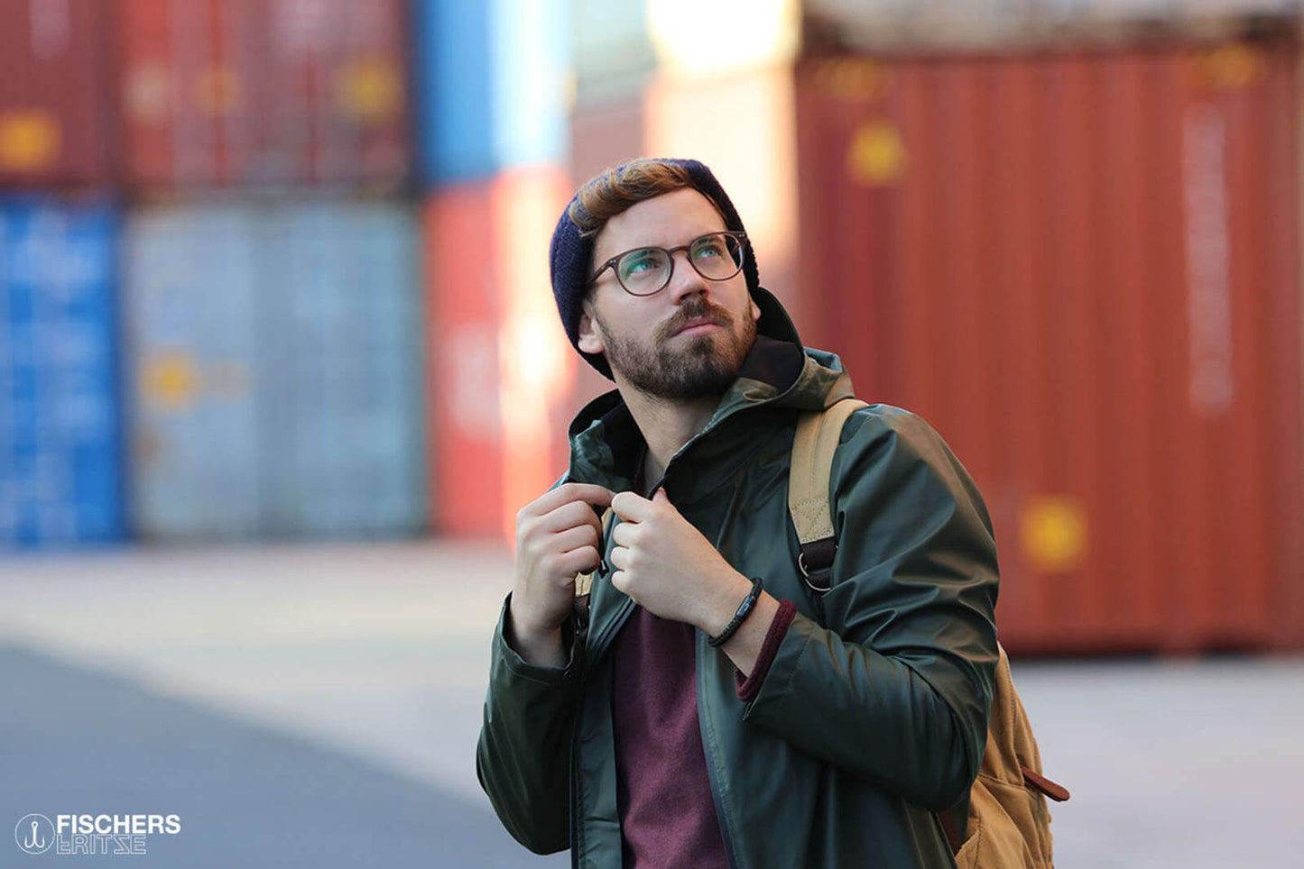 Hip gekleideter, junger Mann spaziert zwischen Frachtcontainer, er traegt ein Fischers Fritze Armband am Handgelenk