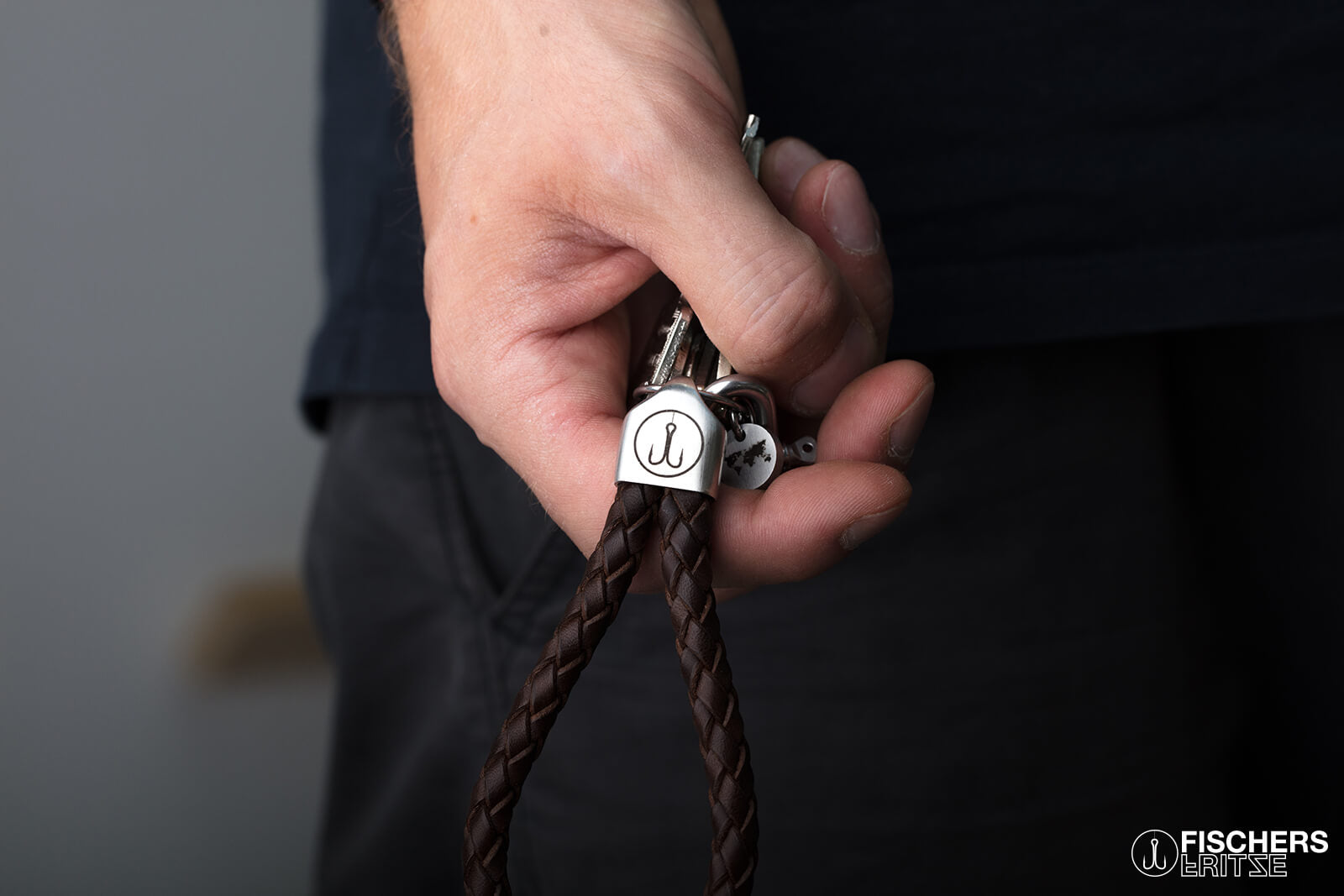 Hand haelt Schluesselanhaenger Leder braun geflochten, Edelstahlfassung mit Gravur sichtbar
