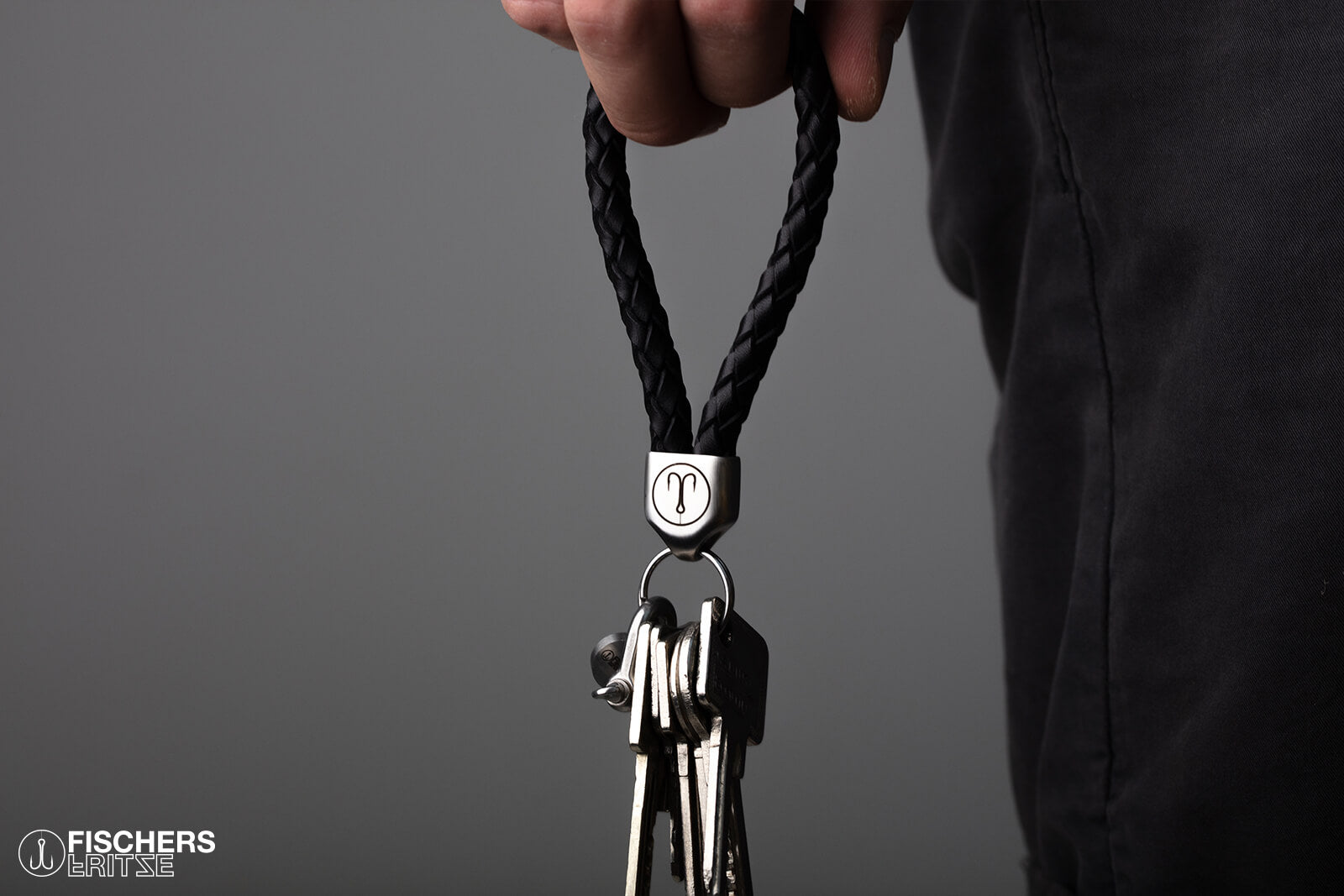 Hand haelt schwarzen Schluesselanhaenger Leder geflochten mit Schluesselbund, Edelstahlfassung mit Gravur sichtbar